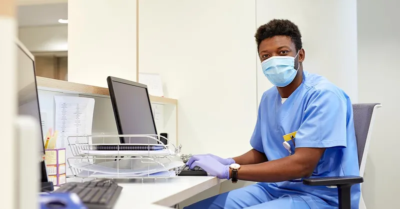Man in scrubs sitting in a medical office at a computer